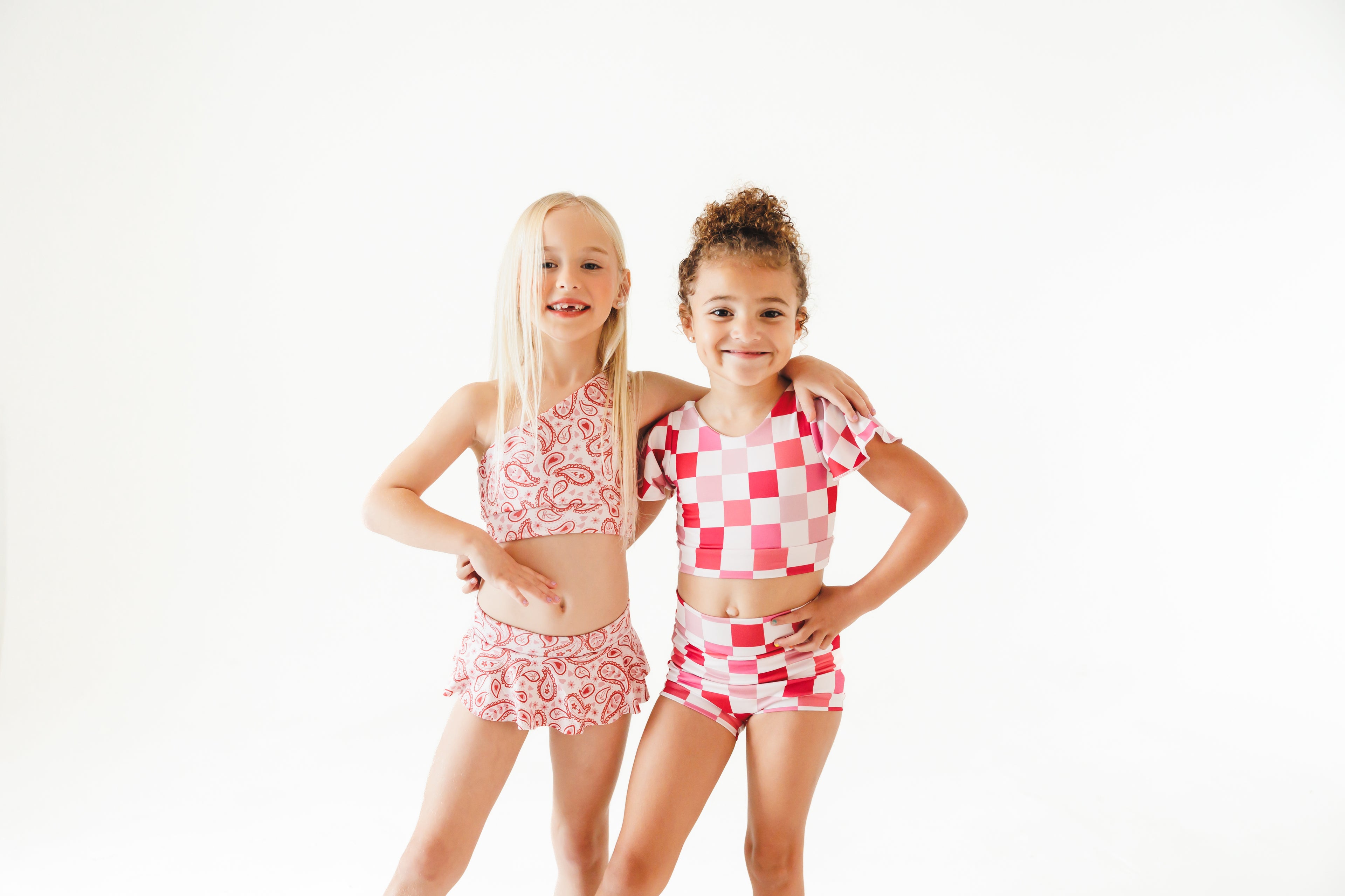 Two young girls wearing matching pink and white dance outfits on a white background